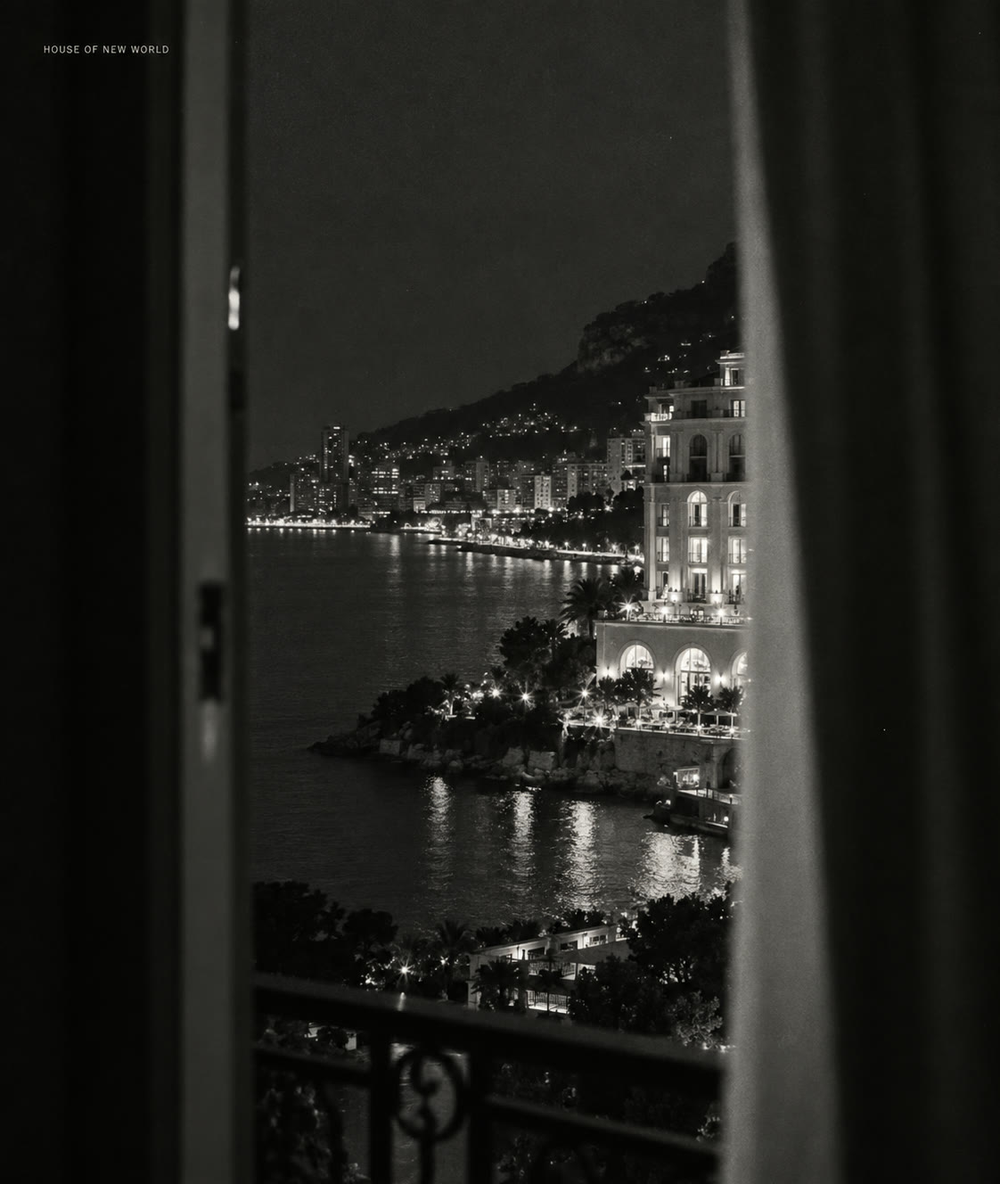 Monte-Carlo Bay at night seen between a door frame and a curtain, the lit hotel above the water, in black and white.