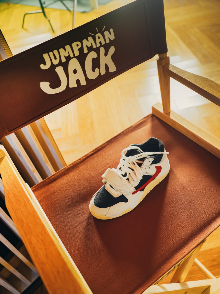 Recess Studios × Travis Scott: a white, black and red sneaker with a hook-and-loop strap on the canvas seat of a wooden director's chair, Jumpman Jack printed on the backrest.
